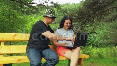 微笑的男人和女人在公园的长凳上用笔记本电脑工作。